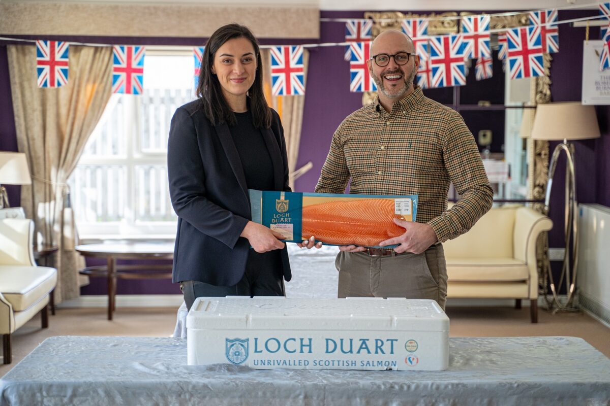 Woman & man stand holding a fillet pack of Loch Duart salmon