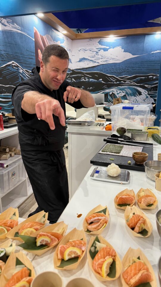 Chef pointing to camera next to prepared sahimi dishes